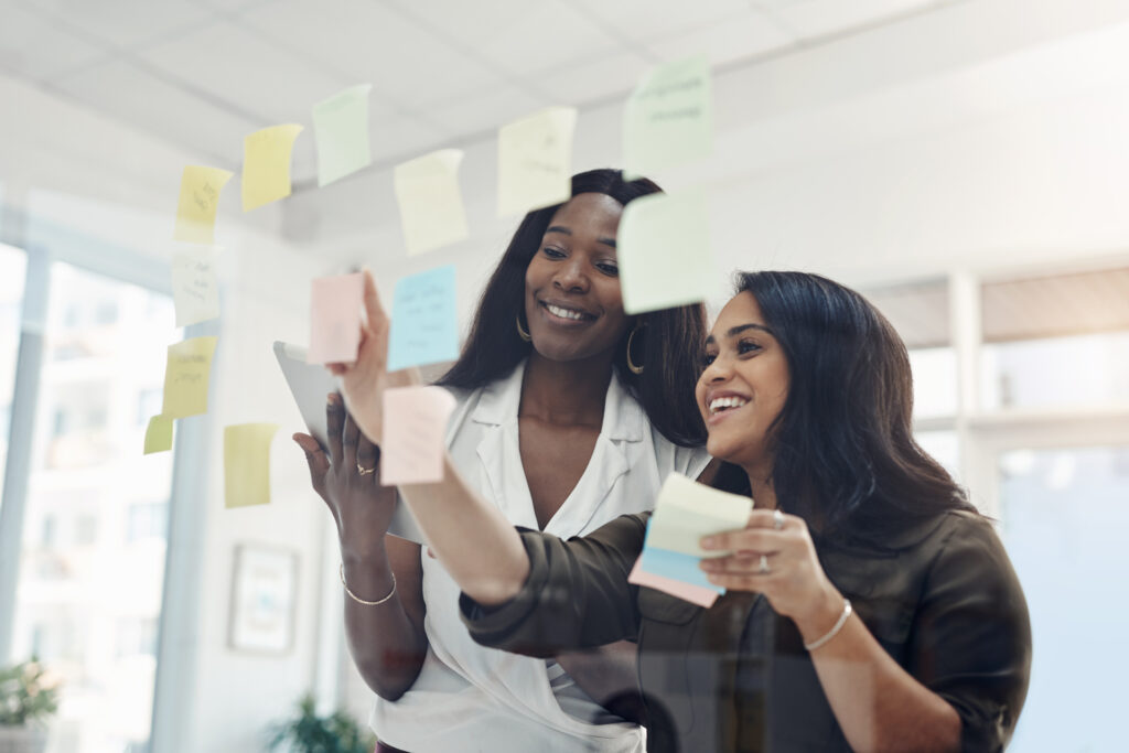 Business always needs a womans touch. two attractive young businesswomen standing together and using a glass board to brainstorm in the office.